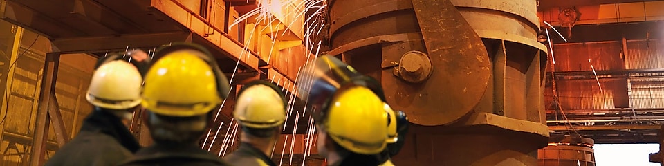 trabajadores mirando maquinaria pesada en una planta metalúrgica
