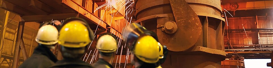 trabajadores mirando maquinaria pesada en una planta metalúrgica