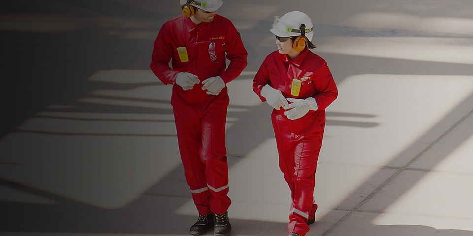Trabajadores y trabajadoras caminando vestidos en monos rojos, con cascos blancos y protección auditiva