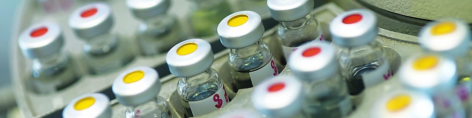 Filas de frascos de medicinas en una gradilla, algunos de ellos con puntos rojos y otros con puntos amarillos en la tapa