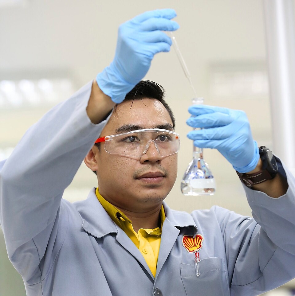 Científicos de Shell con gafas protectoras mientras vierten líquido de una pipeta a una probeta
