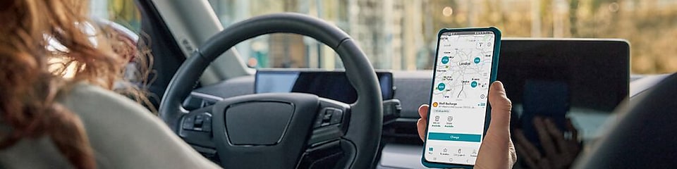 Mano de una mujer dentro de un coche sujetando un teléfono móvil con la app de recarga abierta
