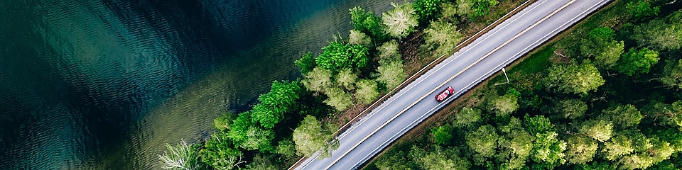 Fotografia aérea de un vehículo rojo en una carretera entre un lago y un bosque. Imagen con texto: Accede a una experiencia de recarga sencilla e intuitiva. 