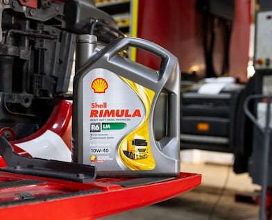 Una botella de aceite para motores diésel de servicio pesado Shell Rimula colocada sobre una pieza roja de camión dentro de un taller.