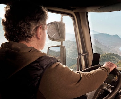 Un conductor de camión manejando por una carretera costera con una vista panorámica de montañas y del mar.