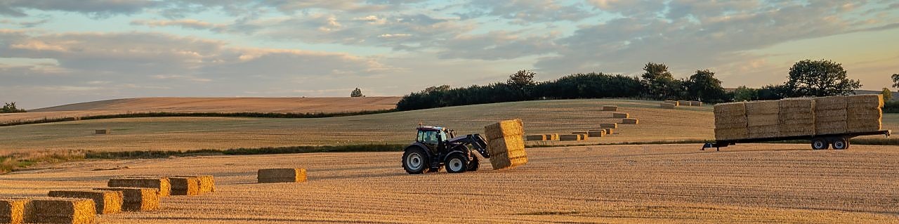 Agricultor recogiendo fardos de heno con un tractor en su granja