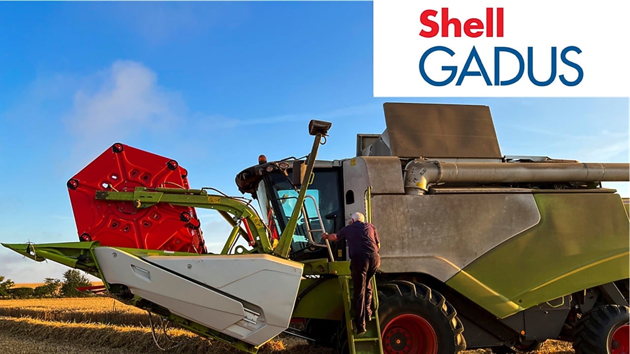 Una persona está subiendo los escalones de una gran cosechadora en un campo - Shell Gadus Greases
