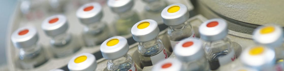 Filas de frascos de medicinas en una gradilla, algunos de ellos con puntos rojos y otros con puntos amarillos en la tapa