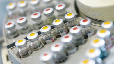 Filas de frascos de medicinas en una gradilla, algunos de ellos con puntos rojos y otros con puntos amarillos en la tapa