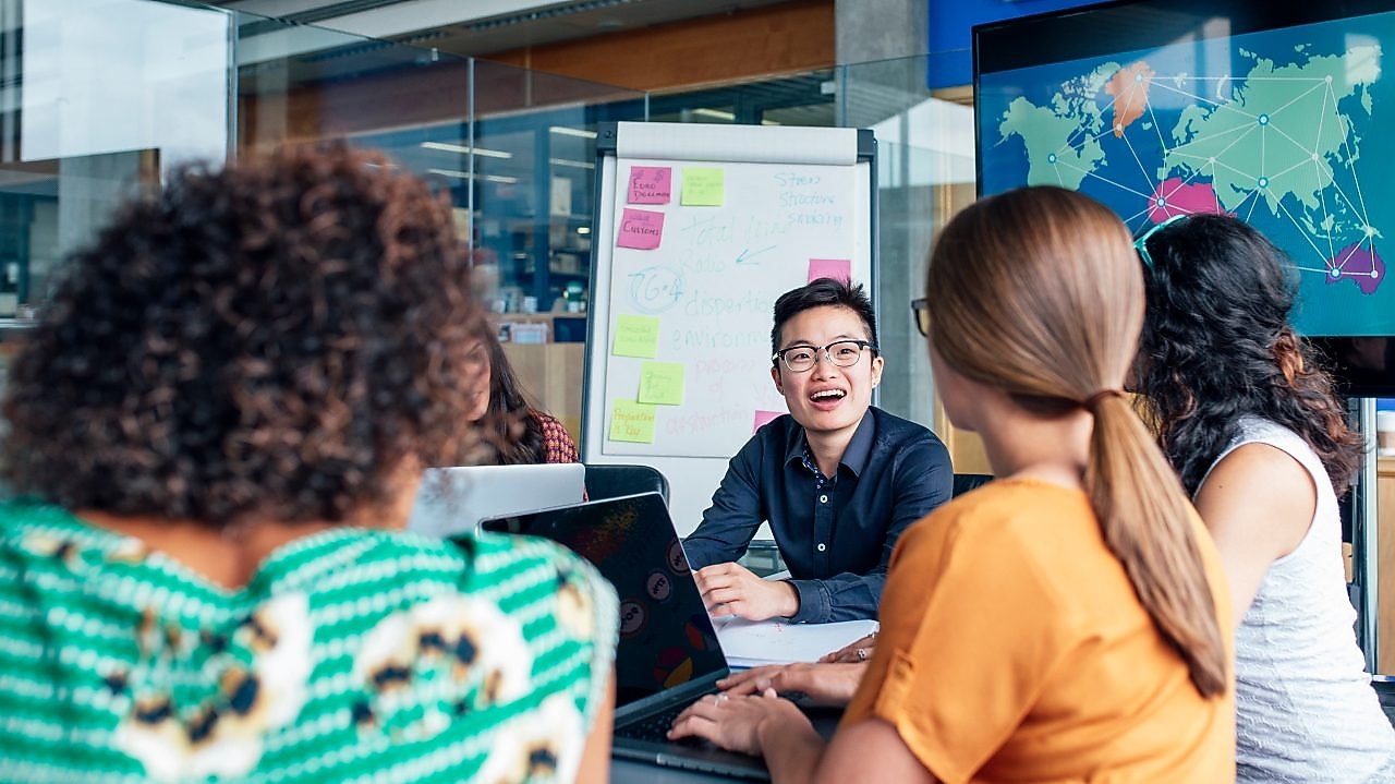 Cuatro hombres de negocios sentados alrededor de una mesa redonda leyendo documentos, alfombra gris y amarilla