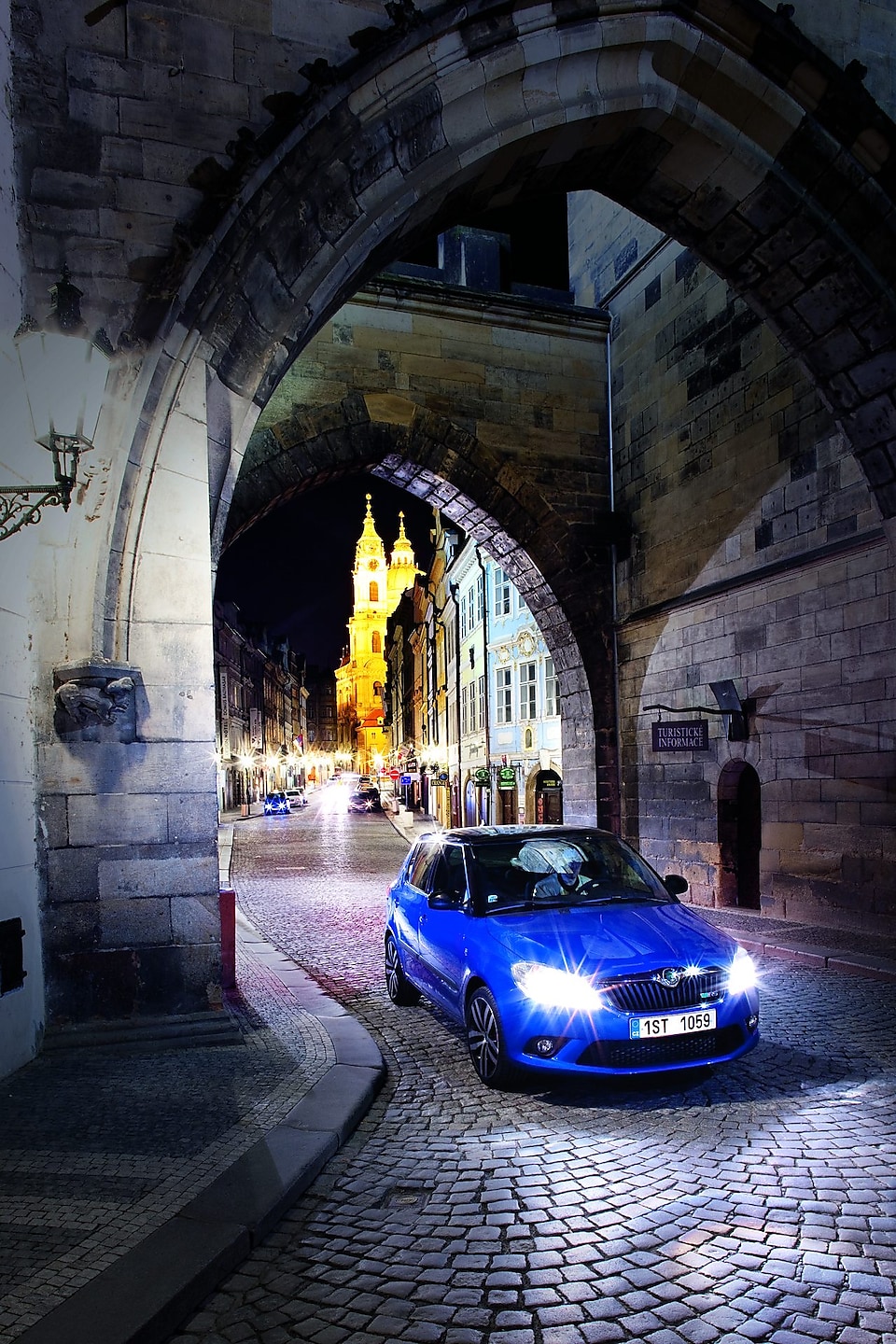 Coche azul aparcado bajo un arco en una calle empedrada de Praga de noche